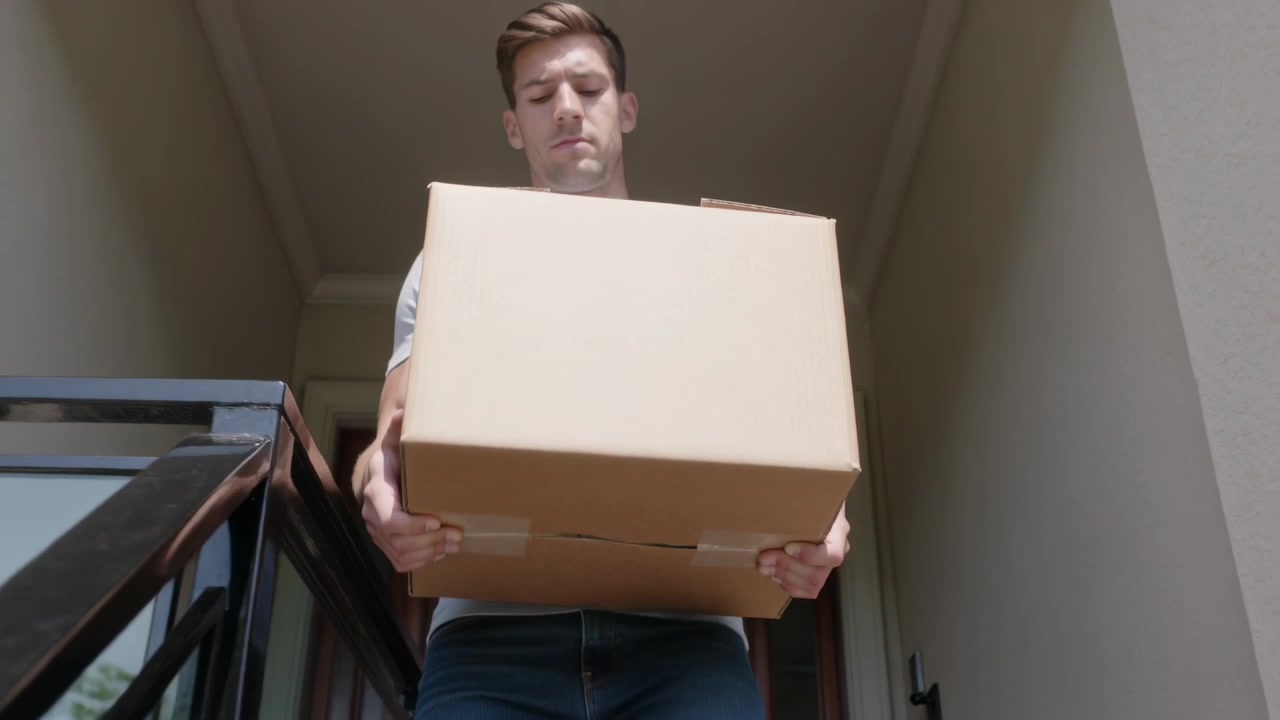Un hombre solo sale de una puerta empotrada, llevando una caja y bajando un paquete por las escaleras, afirmando su agarre.