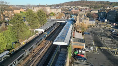 Cinematic-aerial-drone-footage-of-train-parked-in-train-station-with-passengers-leaving-the-train-with-platform-and-carpark-Dewsbury-UK