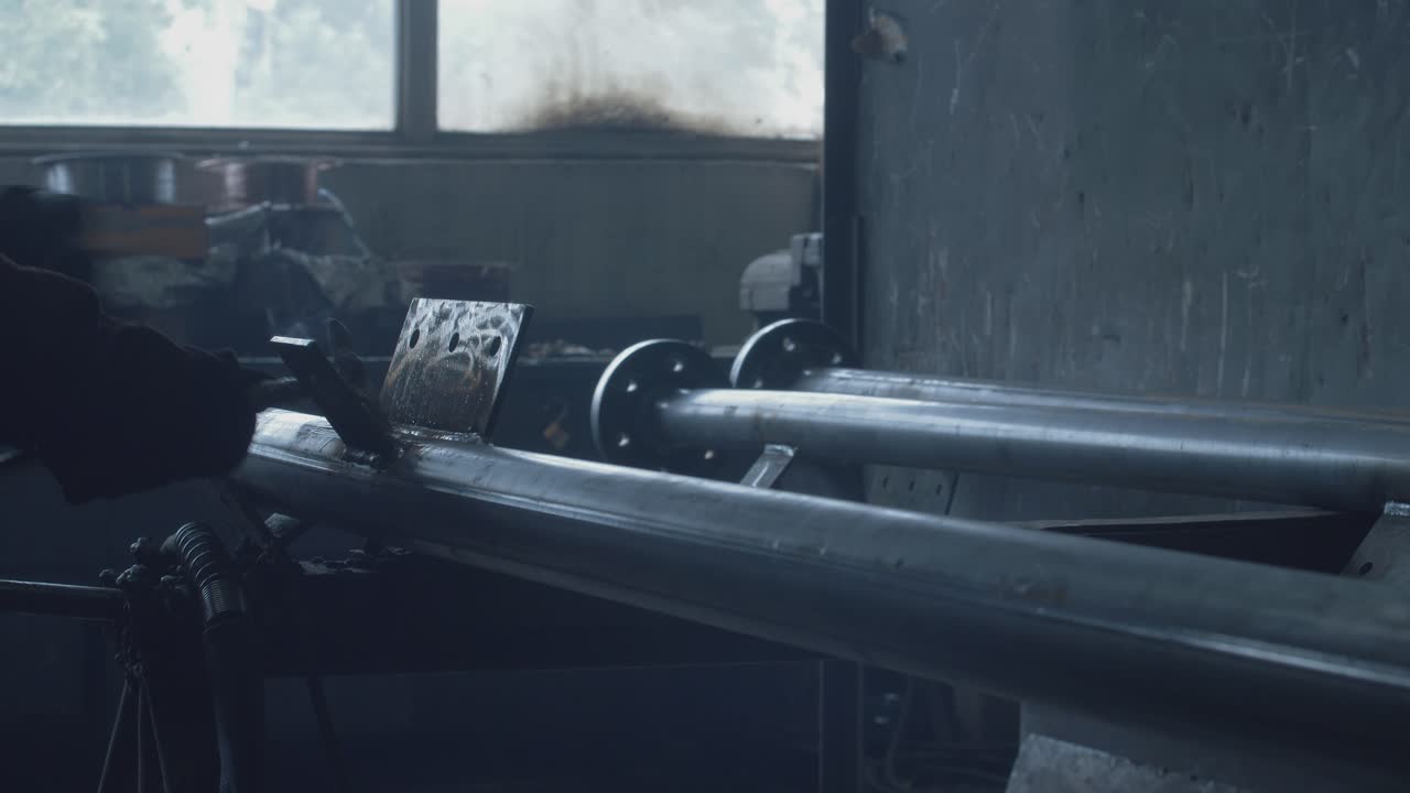 Worker uses metal tool and wire brush to clean the welding spot of a large metal structure.