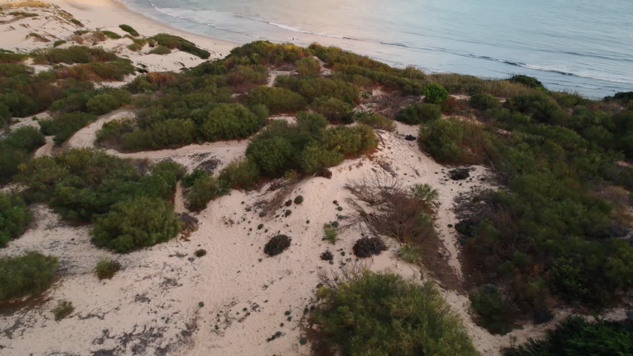 Aufsteigende Luftaufnahme von Sanddünen und der spanischen Küste bei Sonnenuntergang.
