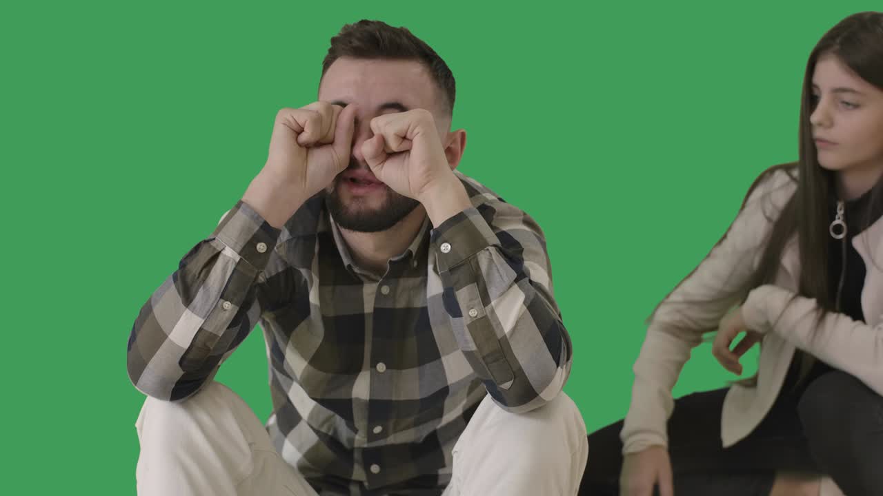 Adolescente surpresa olhando para um homem que esfrega os olhos e chora, fazendo um gesto de 'louco' com o dedo na têmpora. Filha caucasiana morena fazendo um gesto de 'maluco' para o pai triste. Chromakey. Cinema 4k ProRes HQ