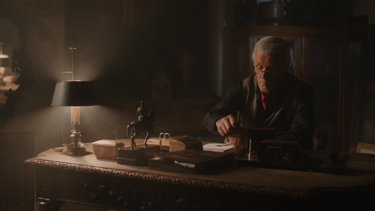 Older passionate man evaluates an old watch in his office at night