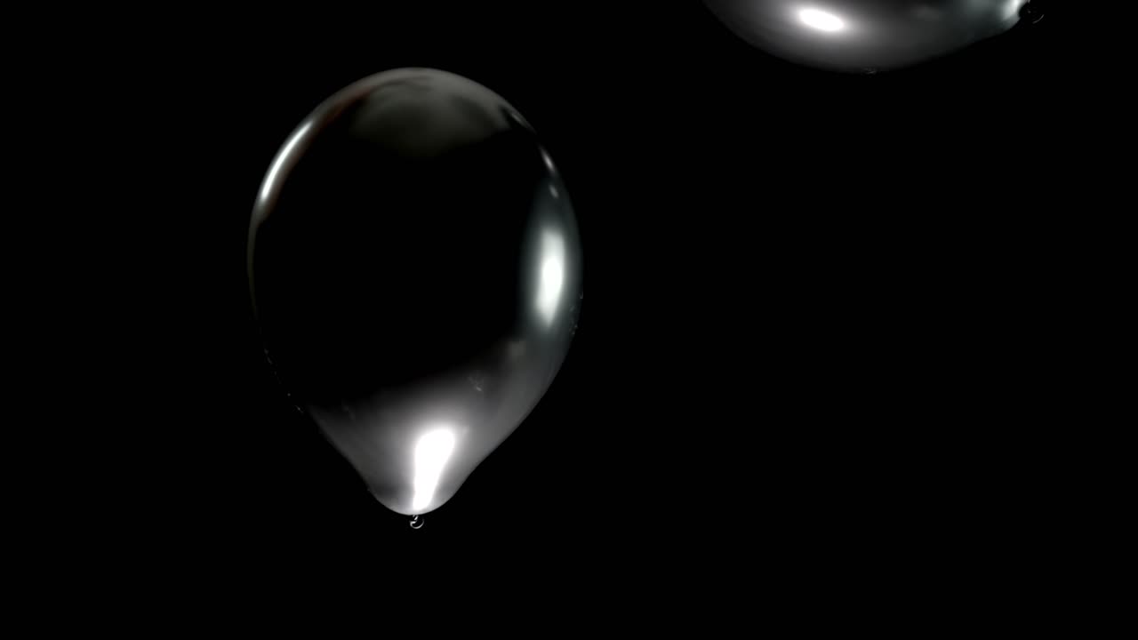 Create a striking visual with this slow-motion clip of two black shining balloons. The black background allows for seamless integration into event videos, perfect for elegant and modern party clips