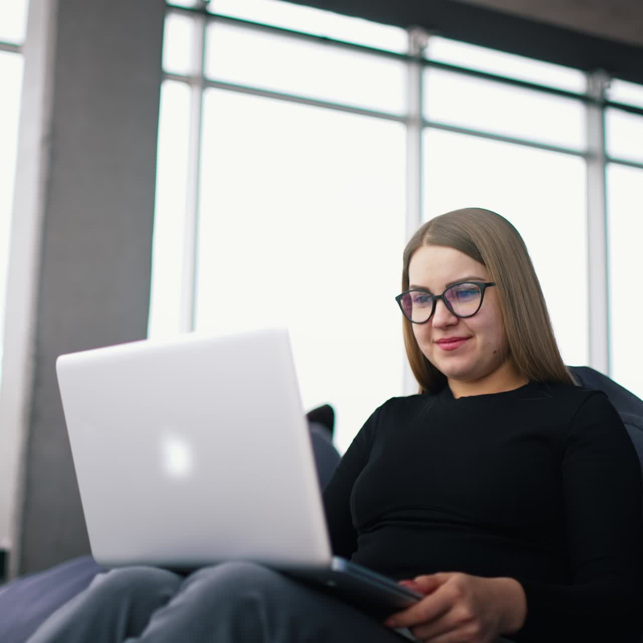 Beautiful young woman in casual clothing using laptop and smiling while working indoors
