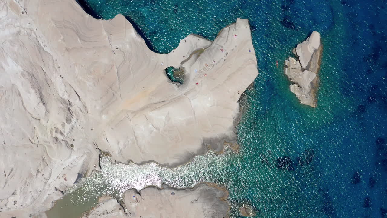aerial: lenta fotografía de arriba hacia abajo de la playa de sarakiniko en la isla de milos, cícladas, grecia con agua de cristal esmeralda durante el mediodía