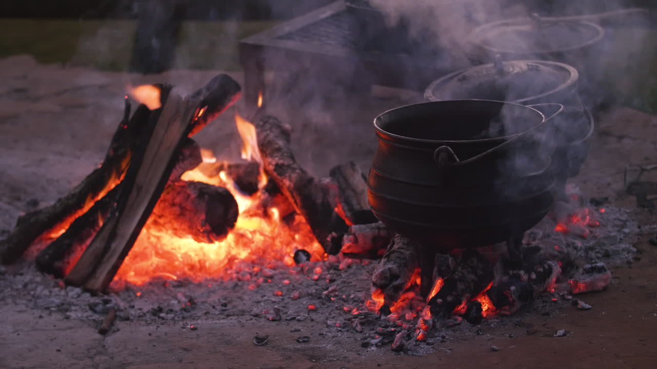 Potjiekos, um prato tradicional sul-africano, cozinhando em uma fogueira aberta à noite.