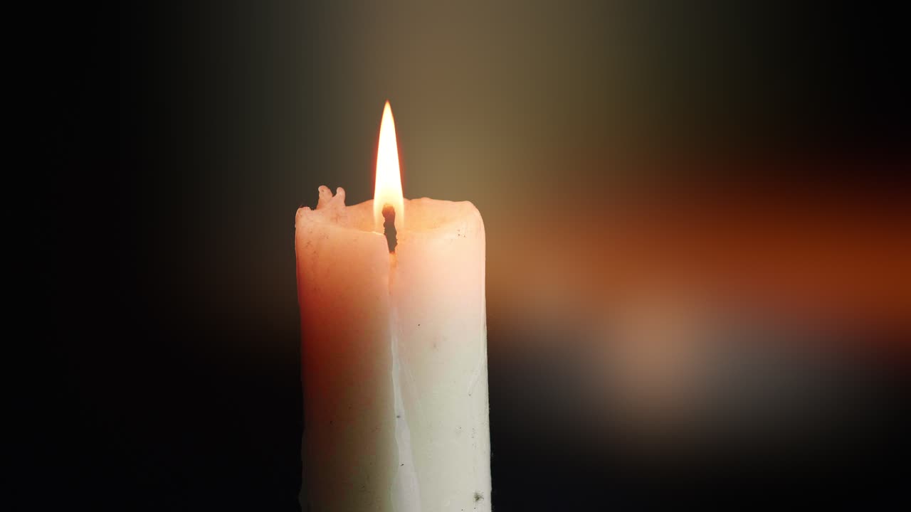 Přehlídka barevných jednotlivých svíček na černém pozadí s efektem světla a zpomaleného pohybu.