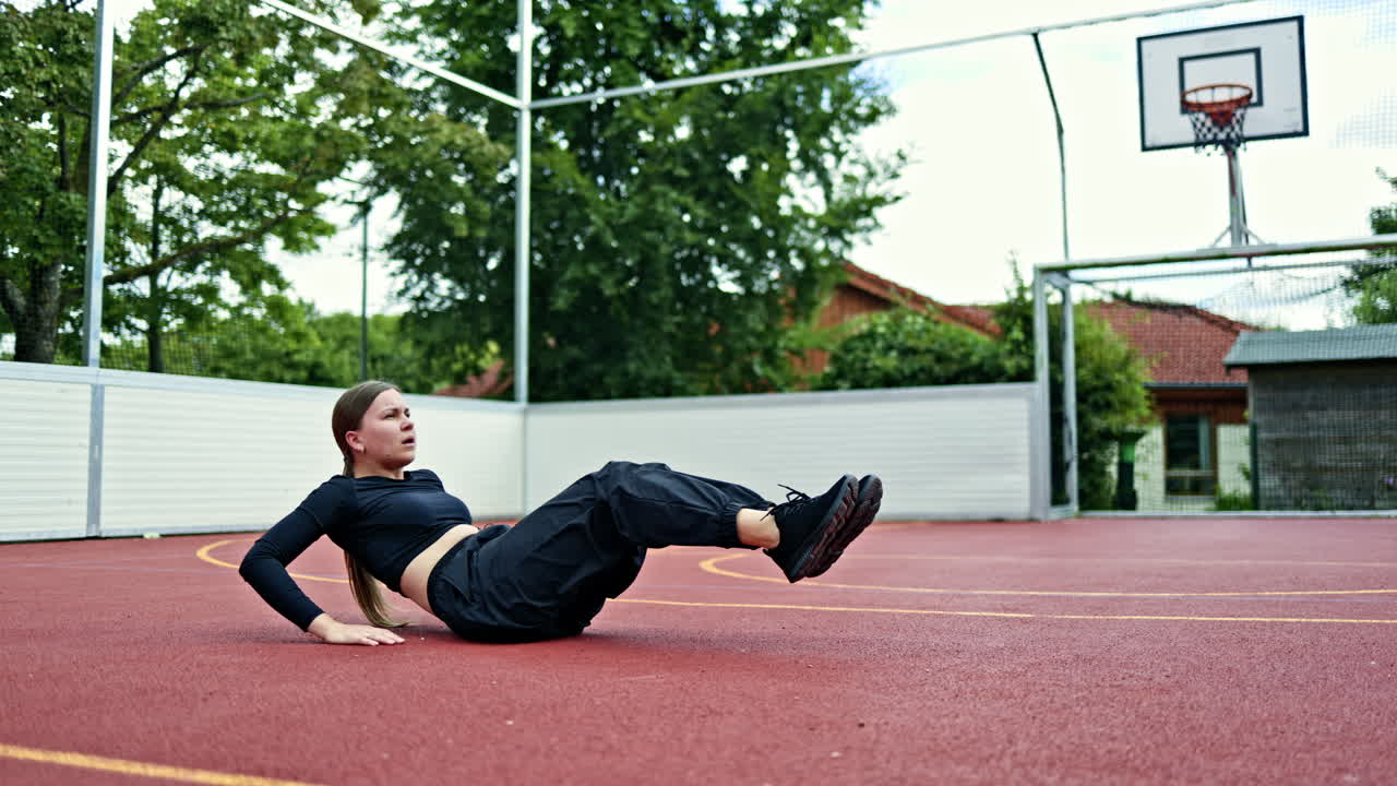 Ung kvinde der laver maveøvelser på en sportsplads i byen. Kvinden dyrker sport i en bypark på jorden. Kvinde i joggingbukser og T-shirt.