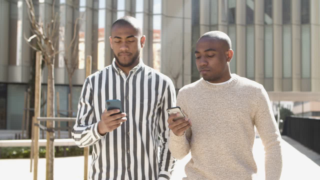 Front view of two thoughtful men walking with phones on street