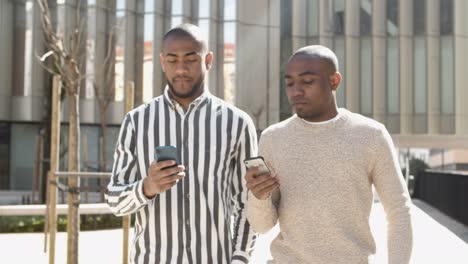 Front-view-of-two-thoughtful-men-walking-with-phones-on-street