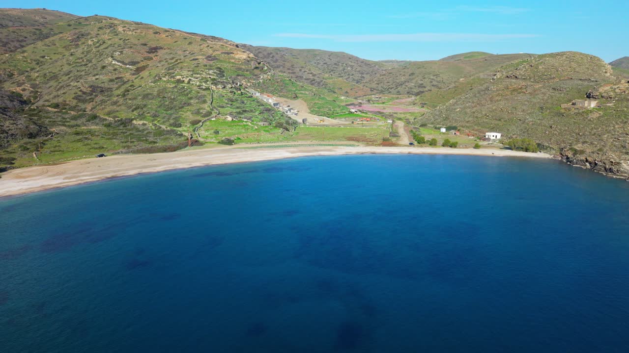 Wide aerial of blue bay next to Kythnos coastline, steep slopes and calm water in daylight