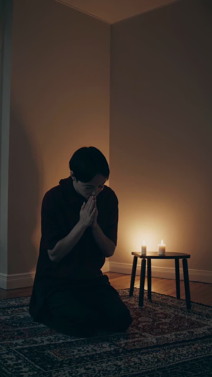 A contemplative scene with a person kneeling in dim candlelight, captured from a low angle