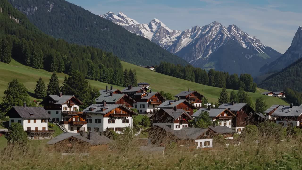 Scenic video of alpine village with rustic houses, lush greenery, and snow-capped mountains