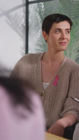 Vertical-Video-Of-Young-Woman-Wearing-Pink-Breast-Cancer-Awareness-Ribbon-Meeting-And-Talking-At-Therapy-Support-Group-For-Cancer-Treatment-Patients-With-Counsellor-2