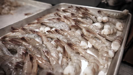 Prepped-shrimp-tails-on-tray,-worker-adds-cleaned-shrimp-to-pile-in-restaurant-kitchen,-slow-motion-close-up-4K