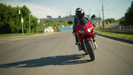 two sisters, both wearing helmets, ride a red power bike while navigating the road, cars can be seen coming from behind, with a blur of city buildings and electric poles along the roadside