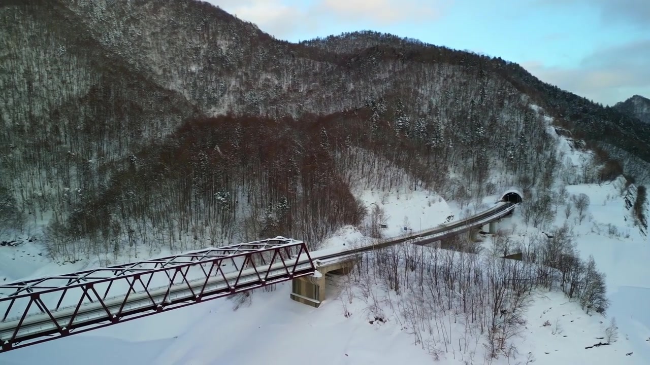 Kinematyczny widok z lotu ptaka na niskiej wysokości na stalowy most kratownicowy prowadzący do tunelu górskiego w zaśnieżonym krajobrazie Hokkaido