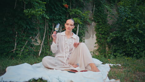 picnic girl drinking wine on grass park. elegant woman sitting blanket at meadow