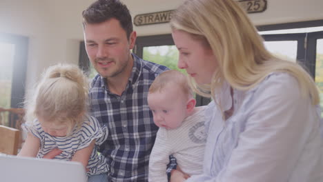 busy family kitchen with father working on laptop with daughter and mother holding baby son - shot in slow motion