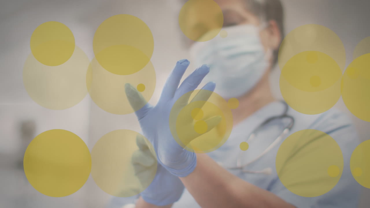 animación de manchas amarillas sobre una doctora caucásica con máscara facial poniéndose guantes.