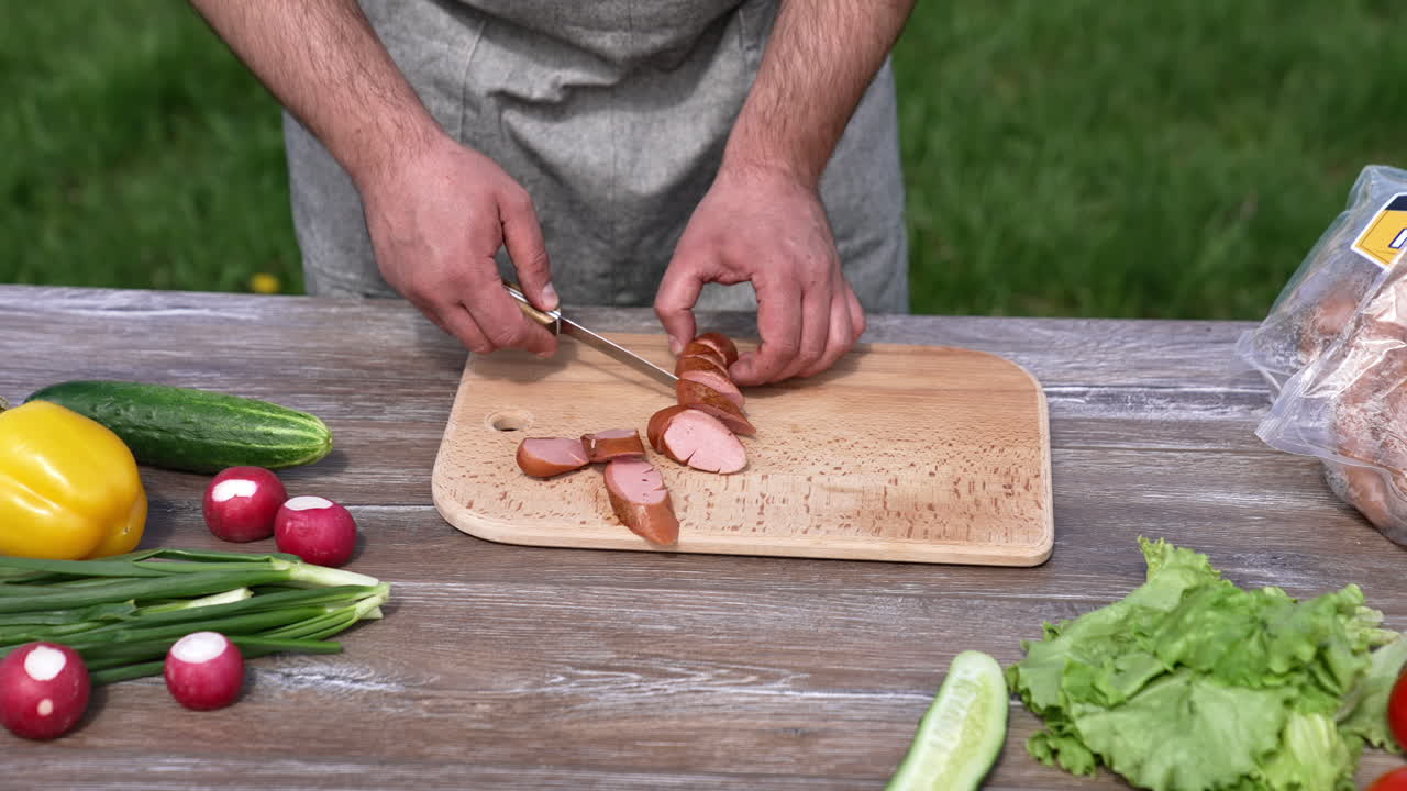 Man cutting barbeque sausage for picnic. Tasty lunch at grill outside.