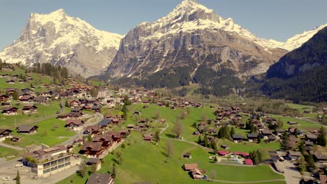 Aerial-drone-footage-raising-down-and-pushing-out-of-Grindelwald-village,-with-train-and-bus-departing