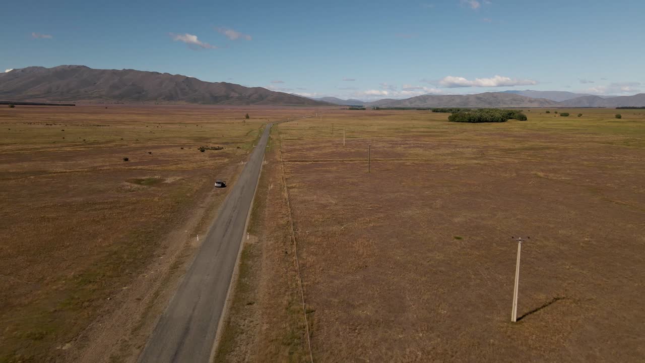 coche abandonado al lado de la carretera de la pradera vacía junto a las líneas eléctricas y las montañas en el fondo