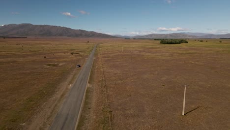 Abandoned-car-on-side-of-empty-prairie-highway-next-to-power-lines-and-mountains-in-background