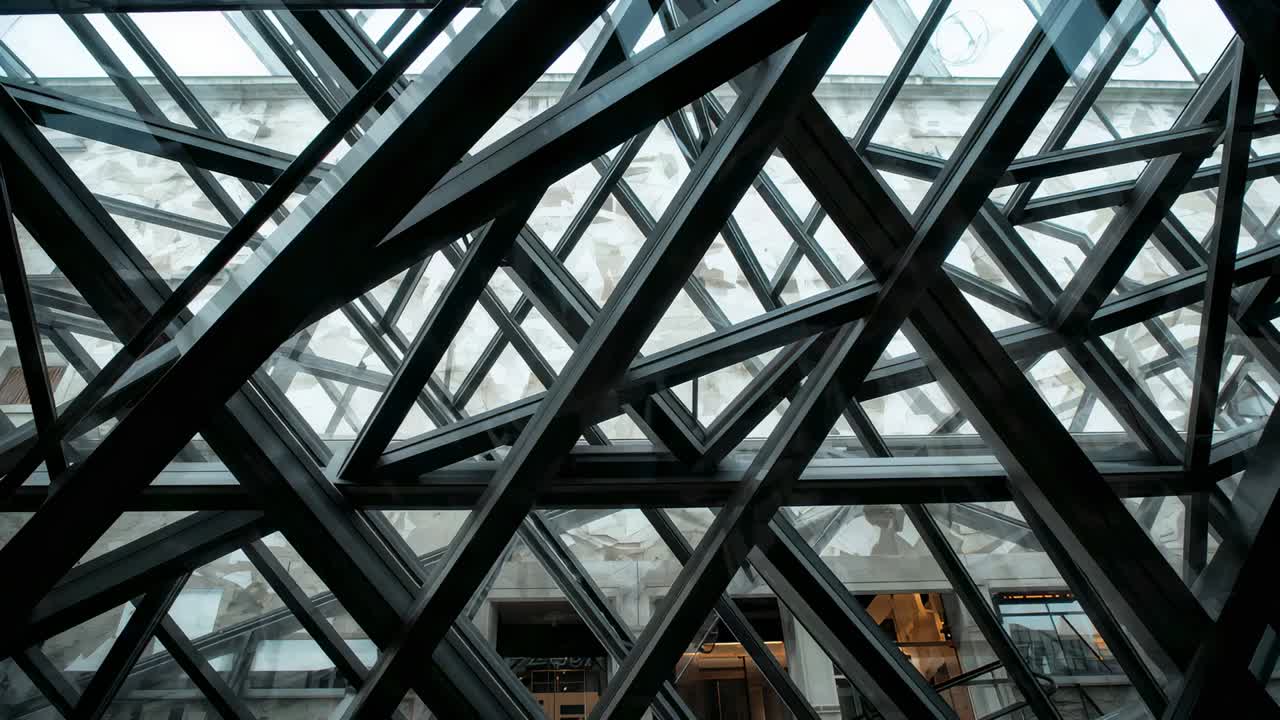 Panning camera revealing crisscross steel lattice at atrium roof, exposing warm shop behind panes