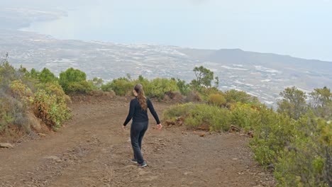 View-over-coast-North-Tenerife,-girl-in-tracksuit-walking-down-trail,-slowmo