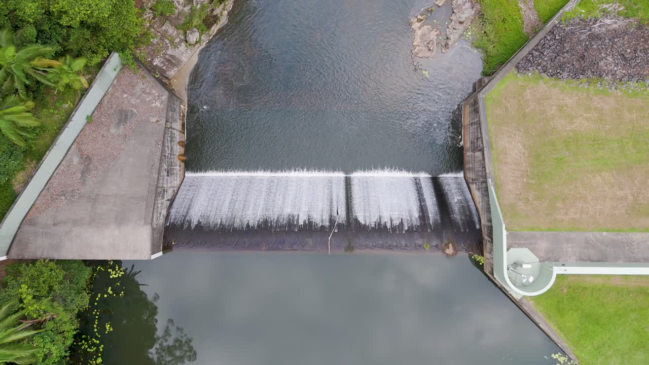 Drone footage captures water flowing over Tullebudgera Dam in Gold Coast, Australia, showcasing lush greenery and serene surroundings