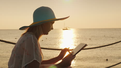 una mujer usa una tableta de vacaciones se sienta contra el fondo del sol naciente sobre el mar siempre