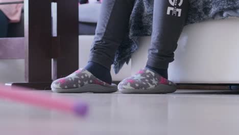 kid wears old women's slippers, and sitting on couch