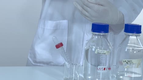 a scientist arranges bottles and a test tube on a lab table, showcasing laboratory preparation.