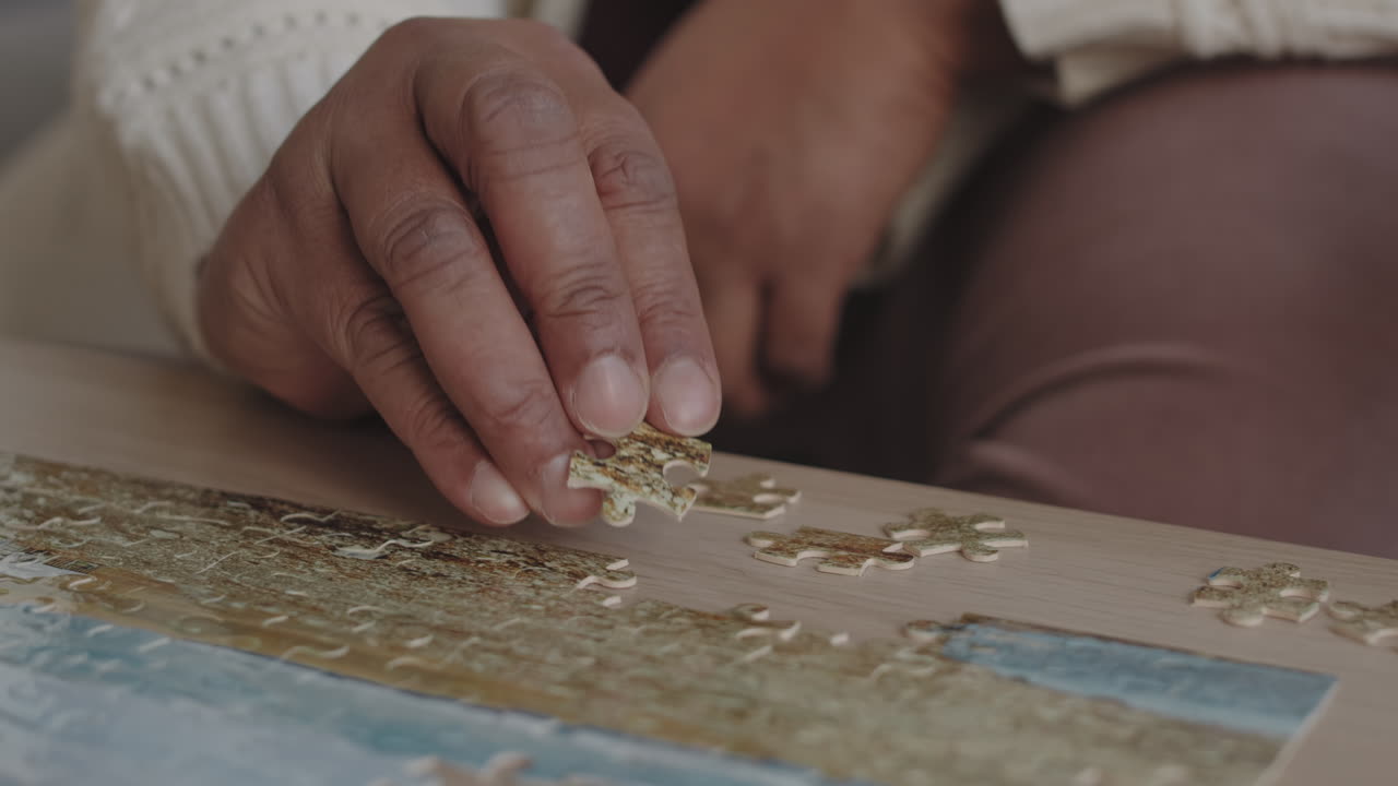Steadicam of hand of cropped unrecognizable person sitting at coffee table, adding piece to jigsaw