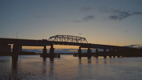timelapse of traffic moving across a truss bridge at sunset in new jersey, with water reflections and fading light creating a cinematic atmosphere.
