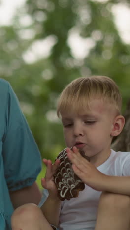 una madre observa atentamente a su hijo pequeño mientras come su bocadillo, mientras que una vista parcial de otra persona se puede ver cerca