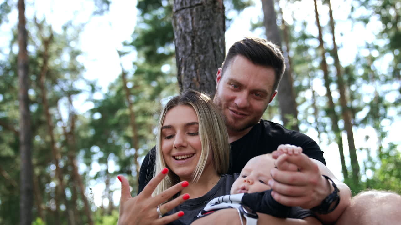 Beautiful Caucasian family of three. Happy people resting in nature with their newborn.
