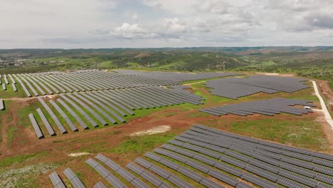 Toma-Aérea-Larga-De-Una-Granja-Solar-Con-Muchas-Filas-De-Paneles-Solares,-En-Una-Zona-Montañosa-En-El-Campo-Portugués