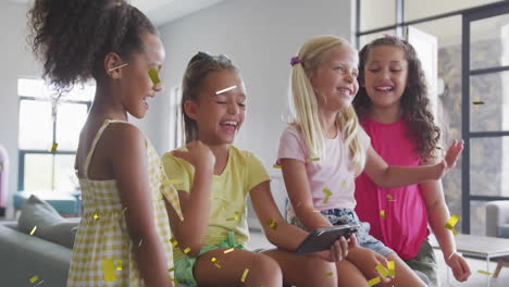 animation of gold confetti over happy diverse schoolgirls using smartphone and laughing in classroom