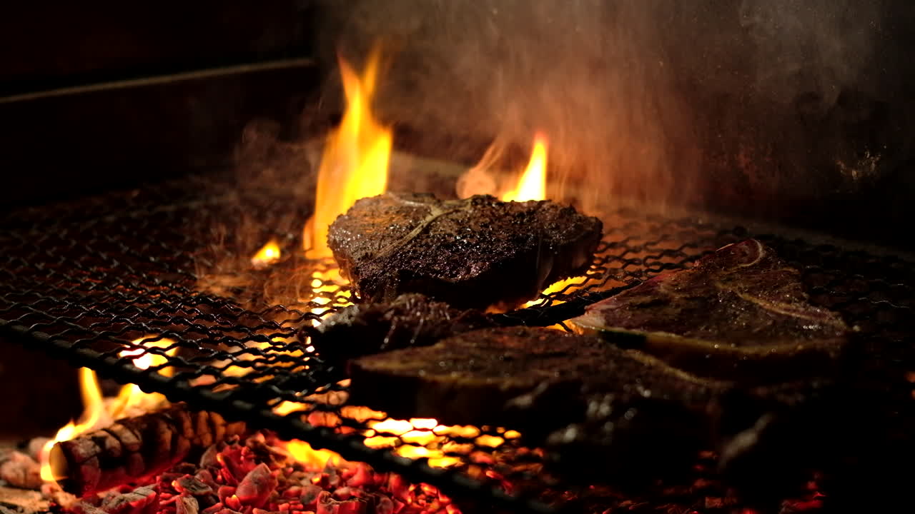 Grilling juicy beef steaks on hot coals of wood fire inside fireplace, telephoto