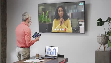 Caucasian-businessman-on-video-call-with-african-american-female-colleague-on-tv-screen