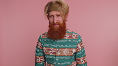 man with red hair and beard wearing a green shirt and headband standing in front of a pink background