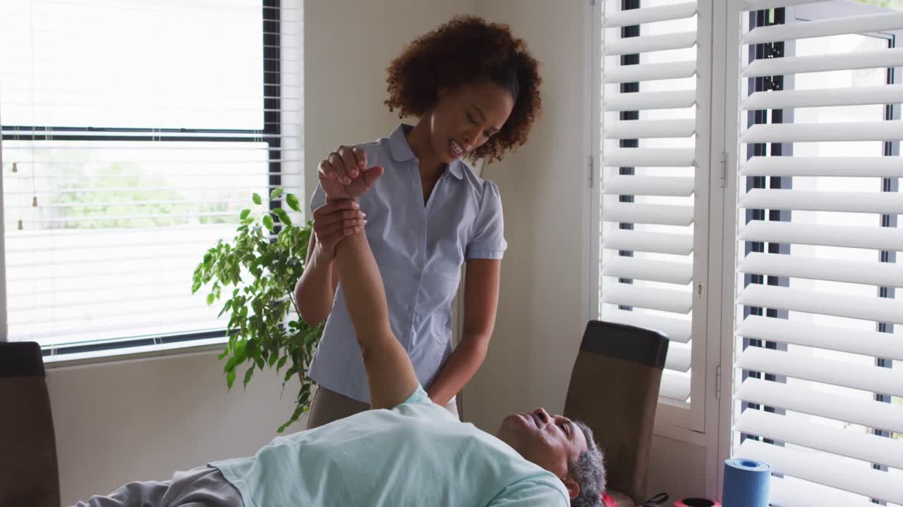 fisioterapeuta de raza mixta ayudando a un hombre mayor estirando su brazo