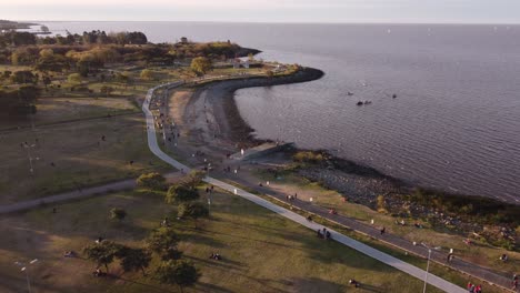 Luftaufnahme-Des-Küstenparks-Vicente-Lopez-Mit-Vielen-Menschen-Und-Dem-Ruhigen-Wasser-Des-Atlantischen-Ozeans-Bei-Sonnenuntergang-–-Panorama-Weitwinkelaufnahme