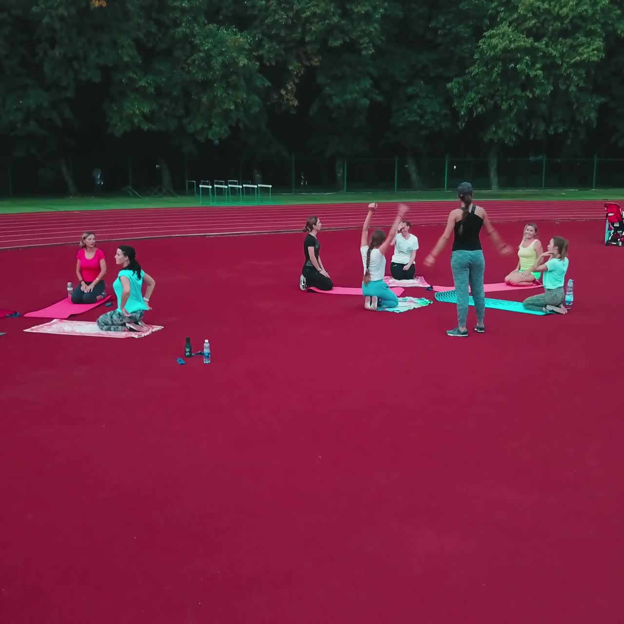 Group of women sitting on mats in the stadium. People doing exercises outdoors in the sports ground.