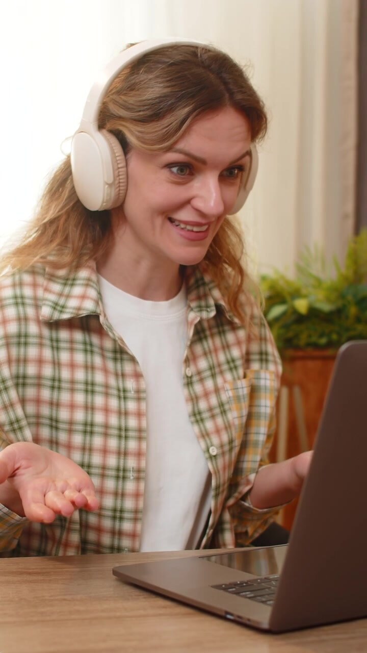 Young woman on home table speaks on laptop video call explaining idea with confident business smile
