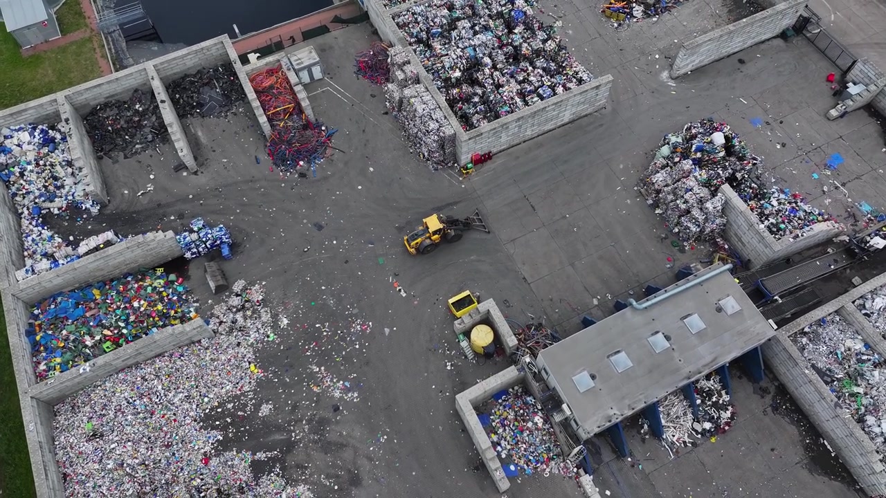 Workers sort and process plastic waste at a recycling facility. Equipment moves materials around. Various types of recyclable plastics are organized and prepared for recovery.