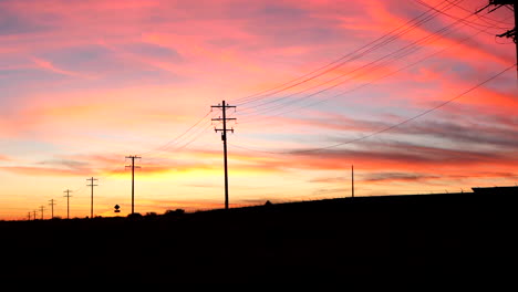 A-colorful-sunset-sky-looking-down-a-country-road-in-the-USA-with-telephone-poles-and-electric-wires-in-silhouette-vanishing-into-the-distance