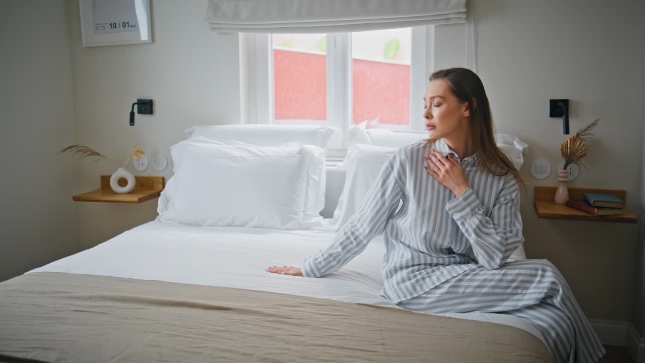 Sad girl sitting bed modern hotel room touching soft white blanket. Upset woman